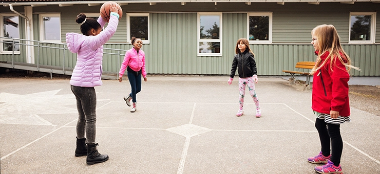 أربعة أطفال يلعبون كرة السلة في فناء المدرسة.