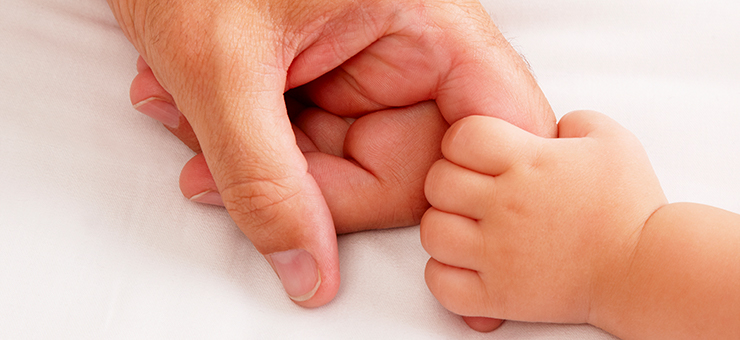 A baby’s small hand is holding an adult’s index finger.