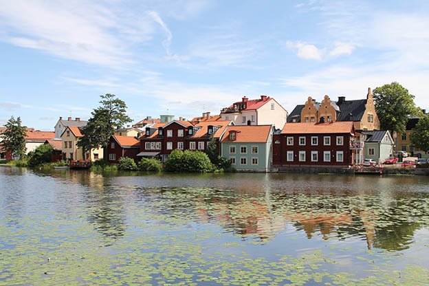 Vy med hus och byggnader i olika färger med träd och buskar vid vatten i centrala Eskilstuna.