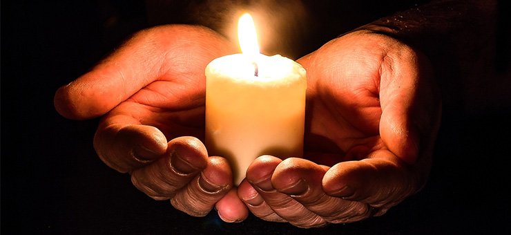 Two hands holding a lighted candle.
