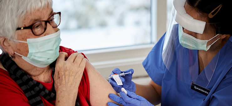 En sjuksköterska vaccinerar en äldre kvinna.