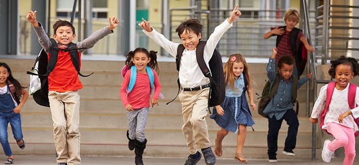 Sju leende och skrattande barn springer mot kameran, några barn har armarna i luften. I bakgrunden syns en stentrappa i skolmiljö.