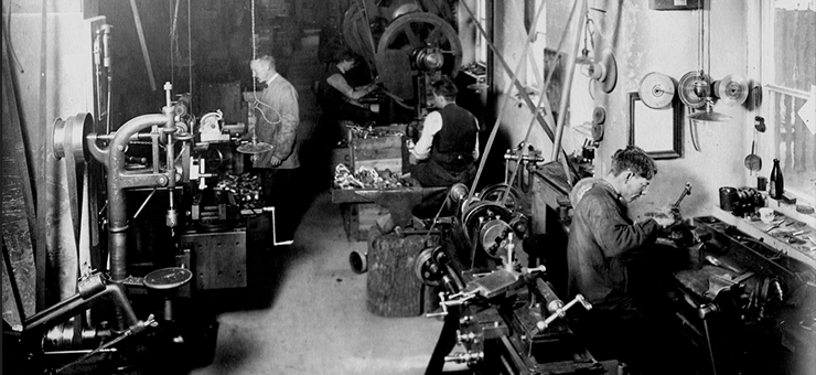 People seated by machines in a mechanical workshop in the 19th century.