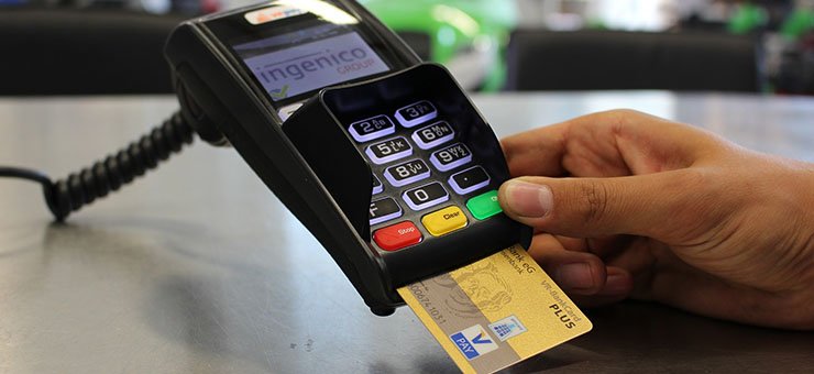 Une main insère une carte bancaire dans un terminal de paiement par carte à la caisse d’un magasin.