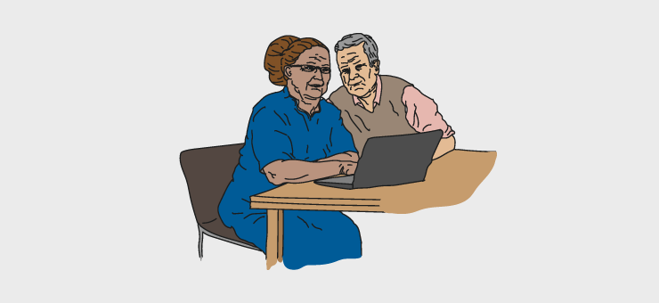 Two elderly people seated at a table in front of a computer.