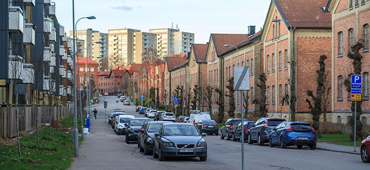A street in a city, with parked cars and both tall and short residential buildings in various colours.